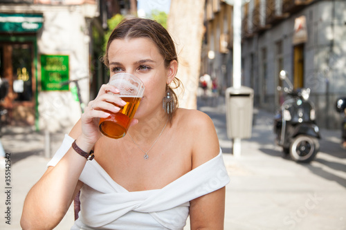 Chica rubia bebiendo cerveza en una terraza de un bar