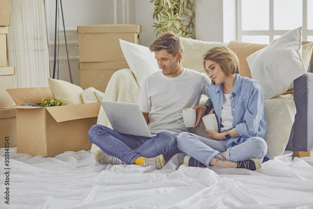 Portrait of happy couple looking at laptop computer together sitting in new house, surrounded with boxes Portrait of happy couple looking at laptop computer together sitting in new house, surrounded with boxes
