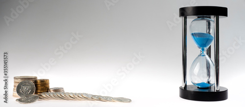 time and money. stacks of coins and an hourglass on a gray background photo