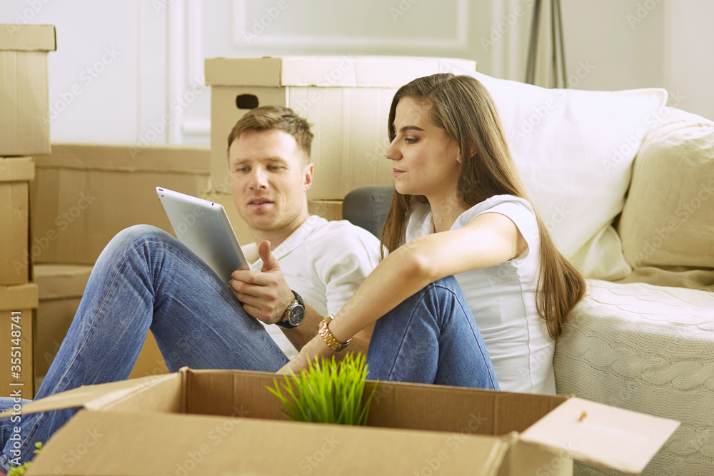 Portrait of happy couple looking at laptop computer together sitting in new house, surrounded with boxes Portrait of happy couple looking at laptop computer together sitting in new house, surrounded with boxes