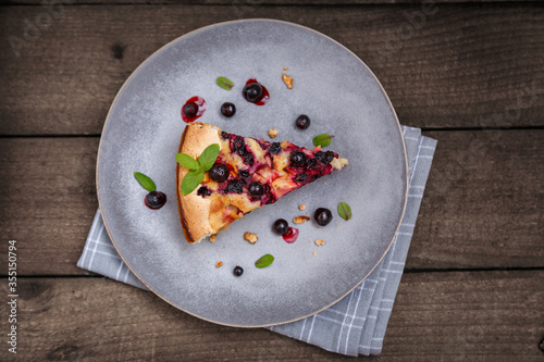 A piece of blackcurrant pie on a grey plate decorated with mint leaves