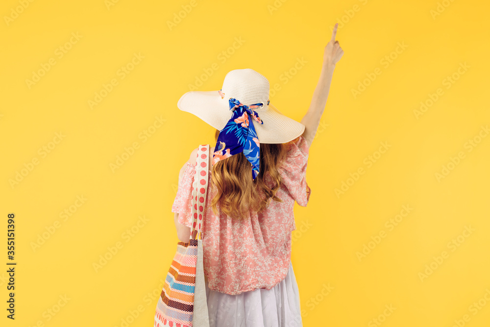 summer young woman in a summer hat, standing with her back to the camera on a yellow background