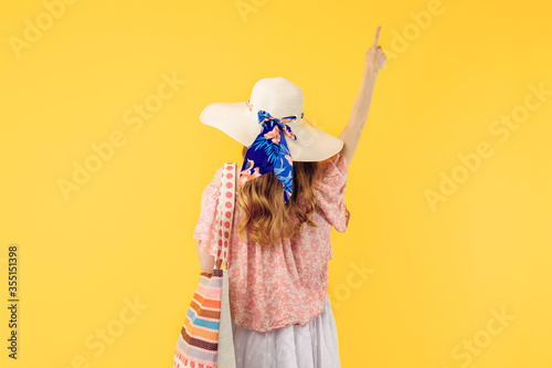 summer young woman in a summer hat, standing with her back to the camera on a yellow background