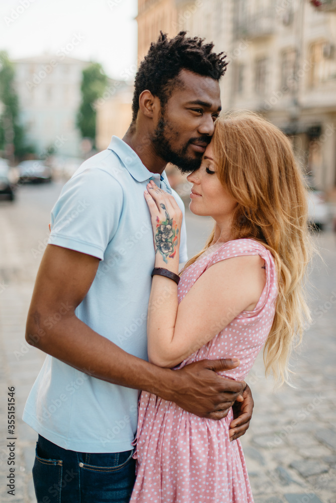 Interracial Relations. An African man and a Caucasian woman stand embracing on a city street.