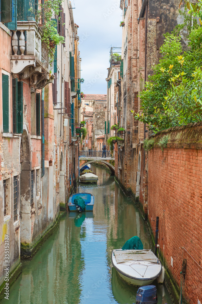 Old quiet venetian street with boats in rainy day. Traditional street in Venice, Italy. Canal with parked boats in Venice