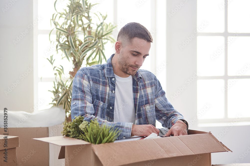 Handsome man with boxes in the new apartment after moving