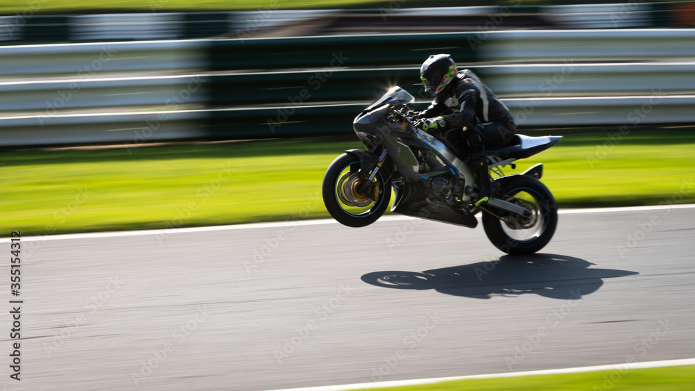A panning shot of a grey racing bike on one wheel as it circuits a track