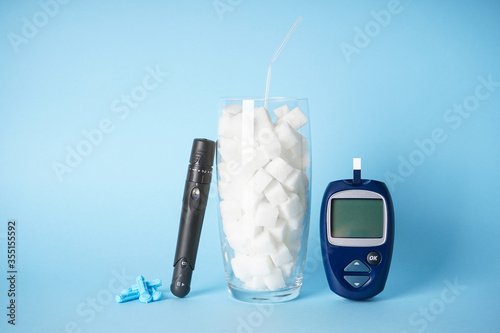 Digital glucometer, lanceolate pen, sugar in a glass on a blue background, close-up. Diabetes concept. photo