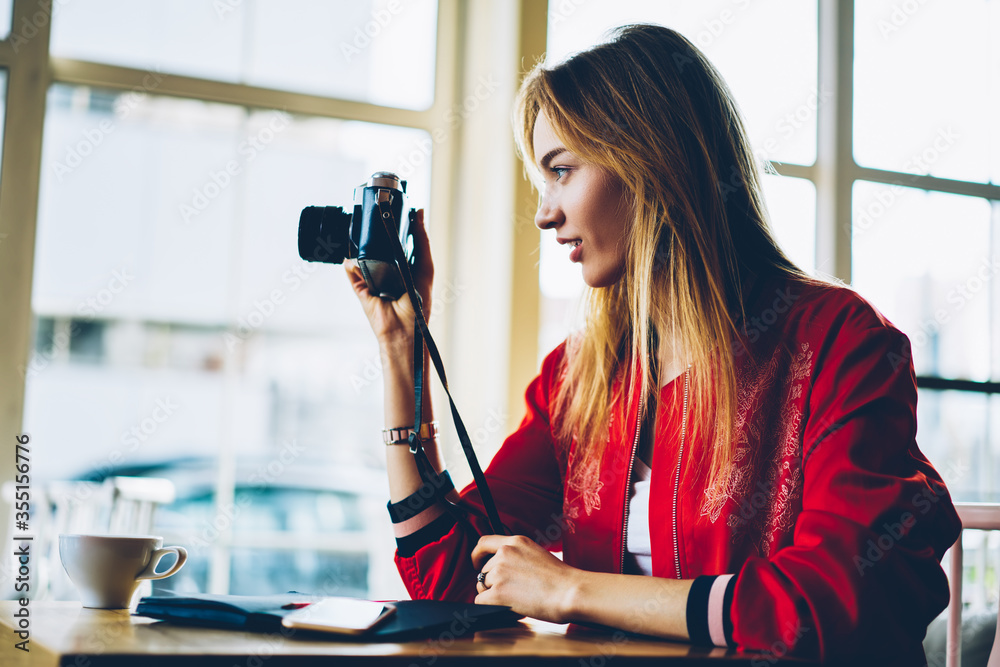Professional female photographer taking picture on old camera focusing lens concentrated on work.Hipster girl fond of photography using vintage equipment making images out of window sitting in cafe Professional female photographer taking picture on old camera focusing lens concentrated on work.Hipster girl fond of photography using vintage equipment making images out of window sitting in cafe