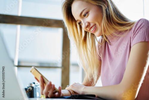 Close up picture of smiling attractive female checking notification on smartphone installing application using wireless connection, smiling female student watching funny videos in socil networks photo