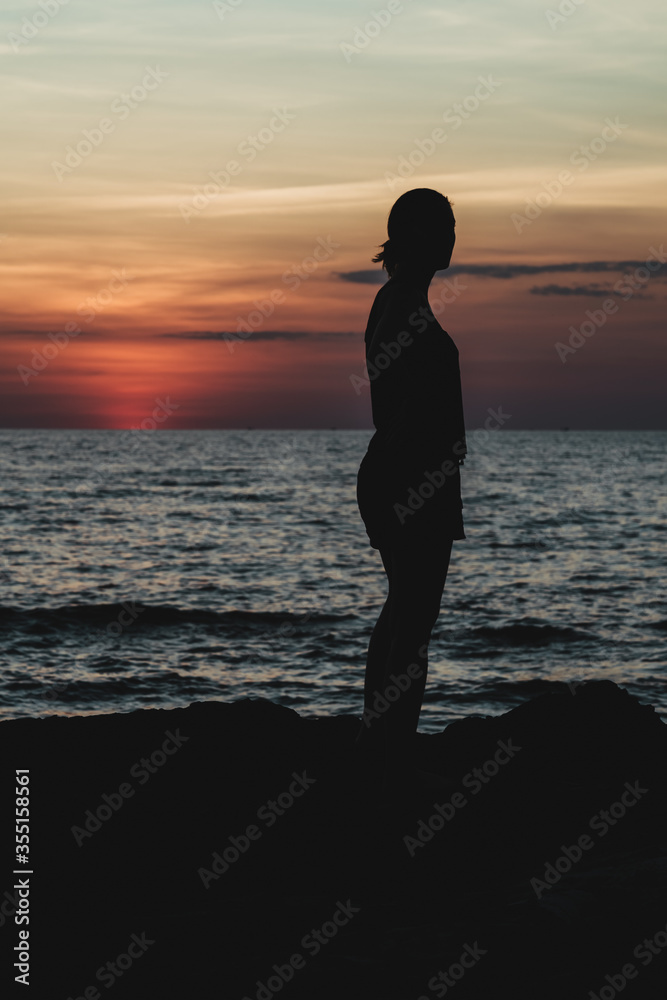 Silhouette of a young woman posing on some rocks on the coast enjoying the sunset.