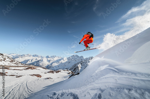 An athlete male skier jumps from a snow-covered slope against the backdrop of a mountain landscape of snow-covered mountains on a sunny day. The concept of winter sports