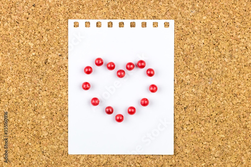 Heart made of red pins attached on a white sheet on a cork board