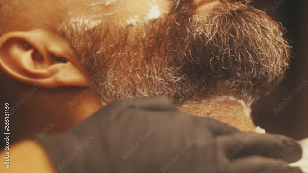 Barber shaving bearded man in barbershop. Male skin care and beard style concept. Close up of hipster male Barber shaving bearded man in barbershop. Male skin care and beard style concept. Close up of hipster male