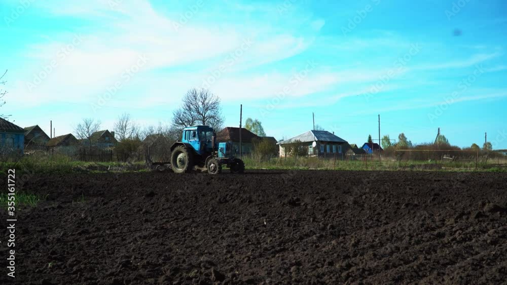 The tractor cultivates and cuts furrows in the field. Tractor work in the black soil field in the village The tractor cultivates and cuts furrows in the field. Tractor work in the black soil field in the village