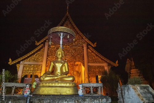 view at night of Golden buddha statue lanna style art with buddhist temple in background, Wat Chedi Luang buddhist temple in Chiang Mai, northern of Thailand.