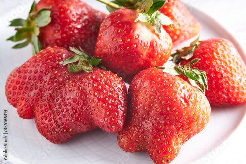 Trendy ugly strawberries in a plate on a light background photo