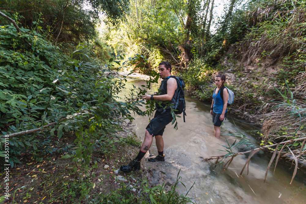 Small group of young tourists walking inside a river with little flow inside a forest in Spain in spring. Selective focus.