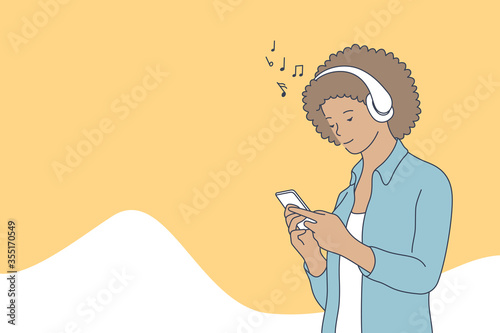 Woman listening music concept. Young happy smiling african american woman holding mobile phone and enjoys musical songs with headphones or play games on smartphone. Leisure time and home recreation.