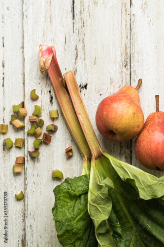 Rhubarb stalks and two pears on a white wooden background. Complementary colors. Grass and fruit