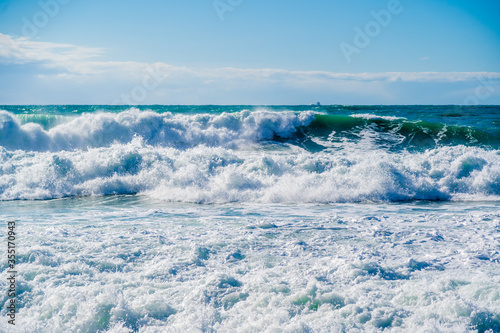 Green waves in white foam and spray rush through the stormy Black sea. The sun shines beautifully on the waves. Dangerous and beautiful. Blue-green gamma