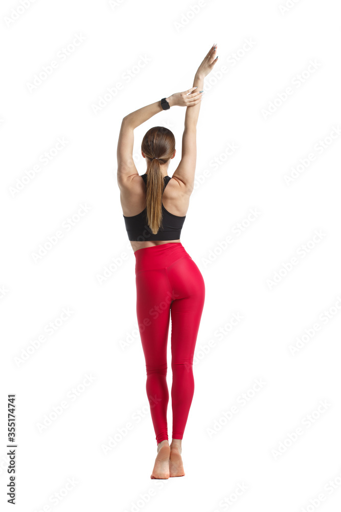 Slender athletic girl in sportswear a black top and pink leggings is  standing in full growth isolated from a white background view from the  back. Stock Photo
