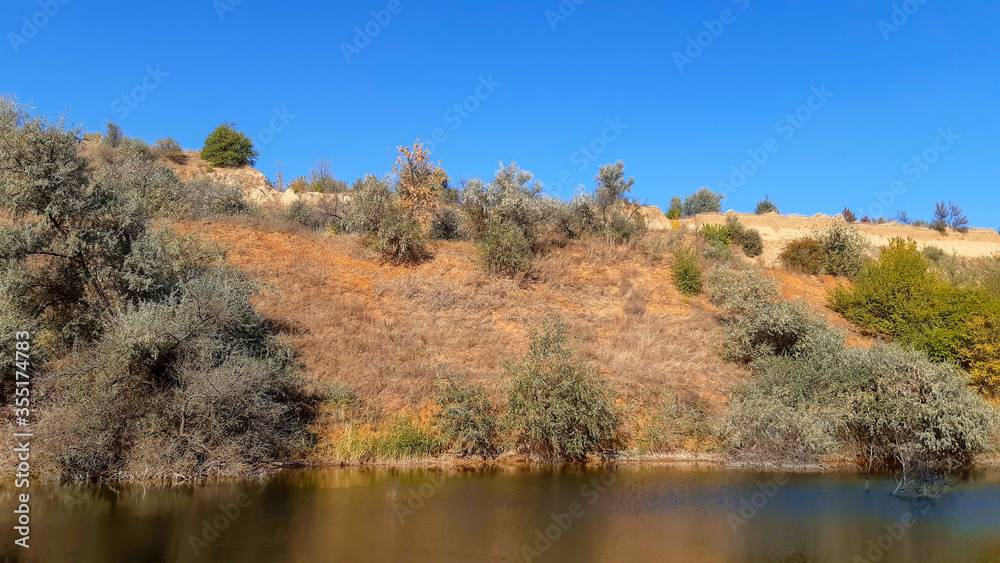 landscape river bank with yellow green trees on a summer day reflected in water landscape river bank with yellow green trees on a summer day reflected in water