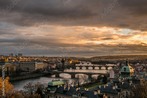 Golden sunset in Prague with dramatic sky from Letna park with Straka academy in the foreground. View of bridges over Vltava with Charles bridge. Czech Republic.