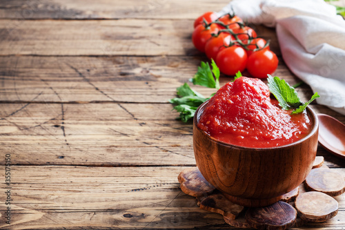 Obraz na plátně Tomatoes in their own juice or Tomato paste in a wooden bowl and fresh tomatoes on a rustic wooden table