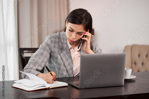 Businesswoman remote homework concept. Woman with a laptop.A young girl talking on the phone and writes in a notebook.