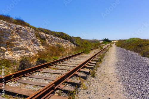 An old messy wooden train track next to stone hill in sunny day in the countryside