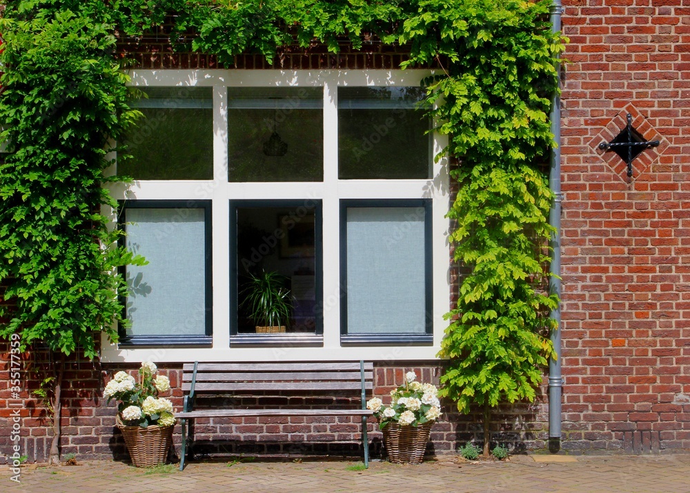 Front of Dutch brick wall house, bench, flowerpots and plants, Netherlands 