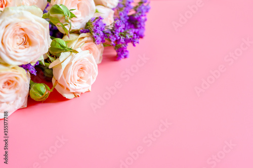 a bouquet of cream roses and bright purple flowers in full bloom on a pink background with space for text. greeting card © Ksenia