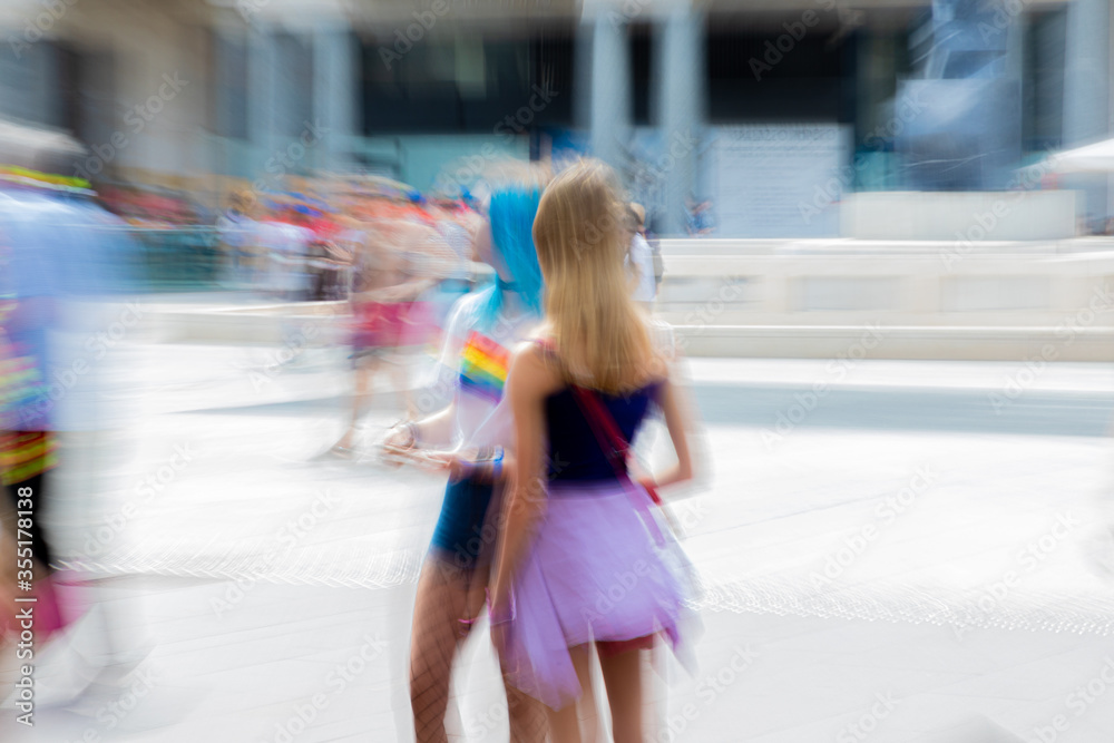 Two young girls await the start of a gay parade (LGBT Pride) on a square in the city. Zoom effect