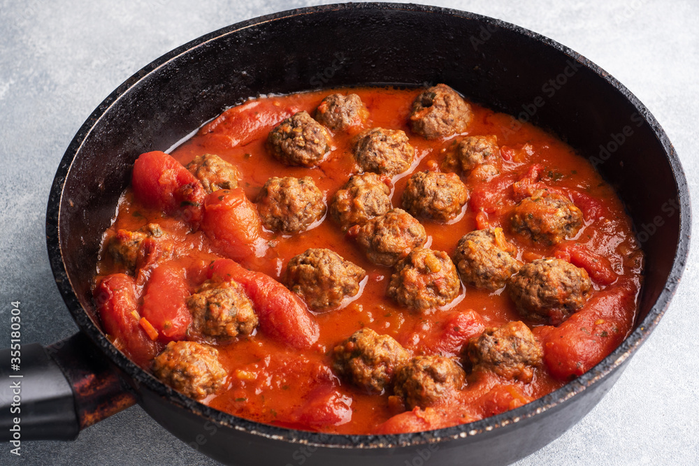Delicious juicy Meatballs in tomato sauce are cooked in a cast iron pan. Close up Concrete background. Delicious juicy Meatballs in tomato sauce are cooked in a cast iron pan. Close up Concrete background.