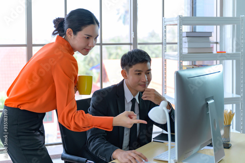 Businessman and businesswoman using laptop computer. Male and female business professional working together in modern office. Business people reviewing paperwork in meeting in modern office.