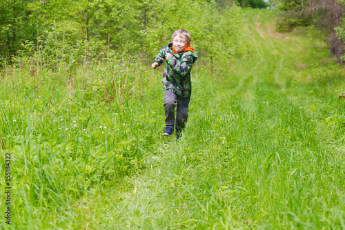 A blond European boy runs along a path in the forest.