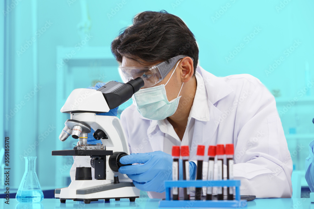 Asian Male Scientist using Microscope working in Lab while Checking Result of Blood Sample testing. Blue Tone. Asian Male Scientist using Microscope working in Lab while Checking Result of Blood Sample testing. Blue Tone.