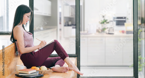 Beautiful asian woman with glasses writing on notebook while sitting in living room. photo