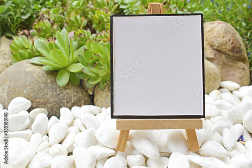 Little wooden tripod with blank canvas in a garden mock up, small wooden easel with blank canvas mockup