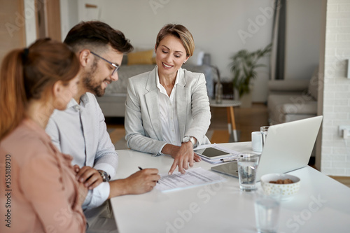 Fototapeta Happy real estate agent showing to a couple where to sign the contract