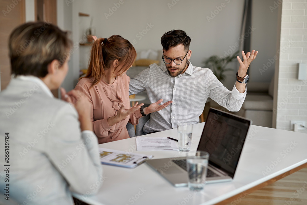 Fototapeta premium Young displeased couple arguing during a meeting with real estate agent.