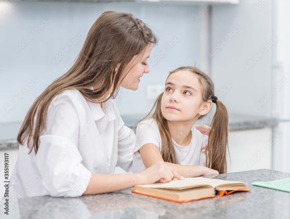 Happy family at home. Young mother and her daughter read a book at home Happy family at home. Young mother and her daughter read a book at home