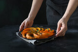 Woman hold slice of pumpkin roasted with thyme and salt. Dark style. Healthy vegan food. Close up.