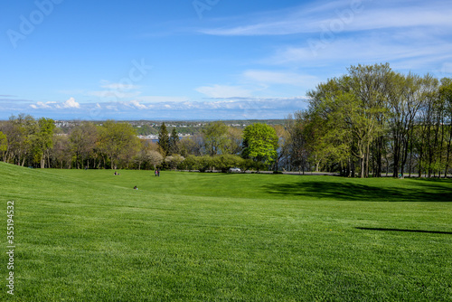 Rolling grassy hill and trees in Battlefields Park with blue sky, clouds and a view overlooking Quebec, Canada.