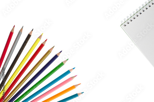 Wooden color pencils on a white isolated background lie like a fan and a notebook.