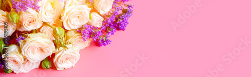 a bouquet of cream roses and bright purple flowers in full bloom on a pink background with space for text. greeting card. flare. banner