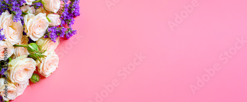 a bouquet of cream roses and bright purple flowers in full bloom on a pink background with space for text. greeting card. banner © Ksenia