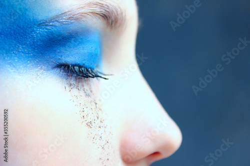 Blurred portrait of young girl with blue make up, close up view. Cropped shot of crying girl.  People, beauty, make up concept.