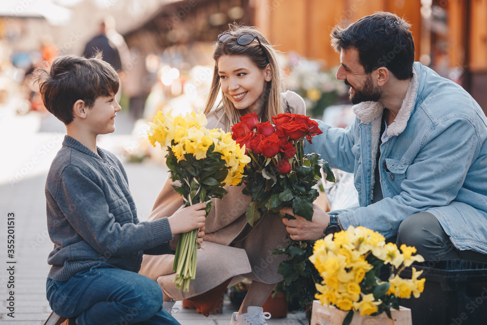 Father, mother and son smiling and looking at eachother while holding flowers